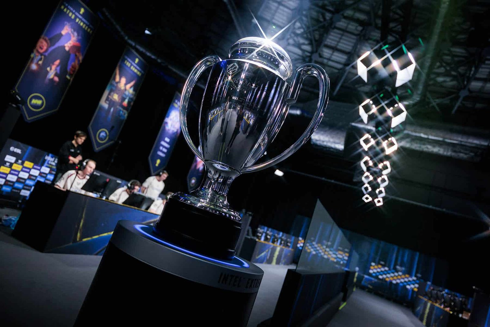 Image of IEM Krakow 2026 trophy placed on stand with esports players competing in background